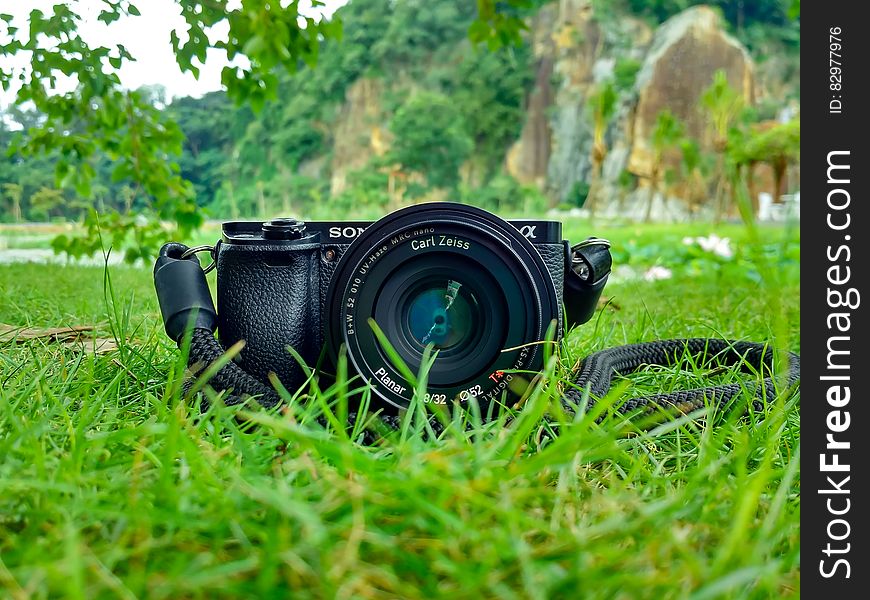 Black Sony Dslr Camera on Green Grass in Front of Brown and Green Mountain