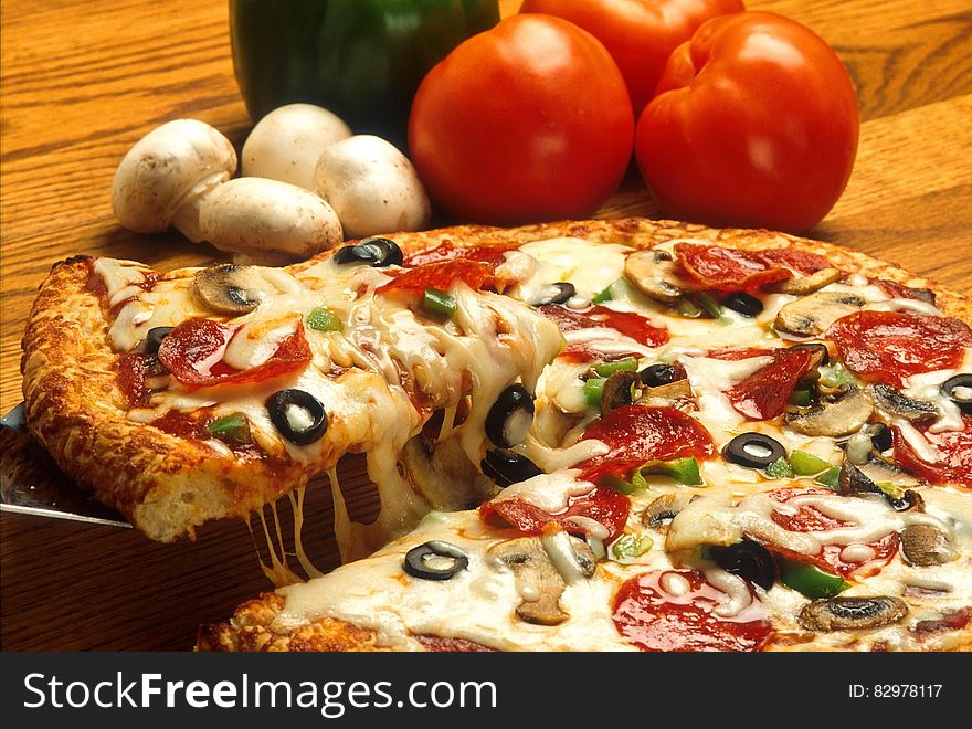 Close up of pizza pie with fresh tomatoes and mushrooms on wooden table. Close up of pizza pie with fresh tomatoes and mushrooms on wooden table.