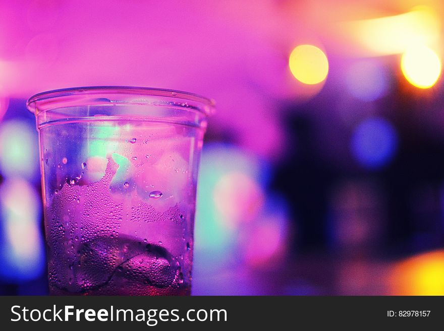 Plastic glass with ice cube on bar with purple lights. Plastic glass with ice cube on bar with purple lights.