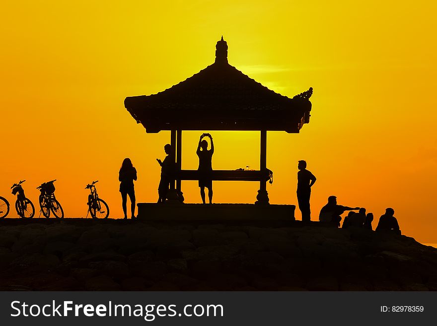 Young people in silhouette on a hilltop with light from a golden sunset and with an Asian style shelter and bicycles propped up nearby. Young people in silhouette on a hilltop with light from a golden sunset and with an Asian style shelter and bicycles propped up nearby.