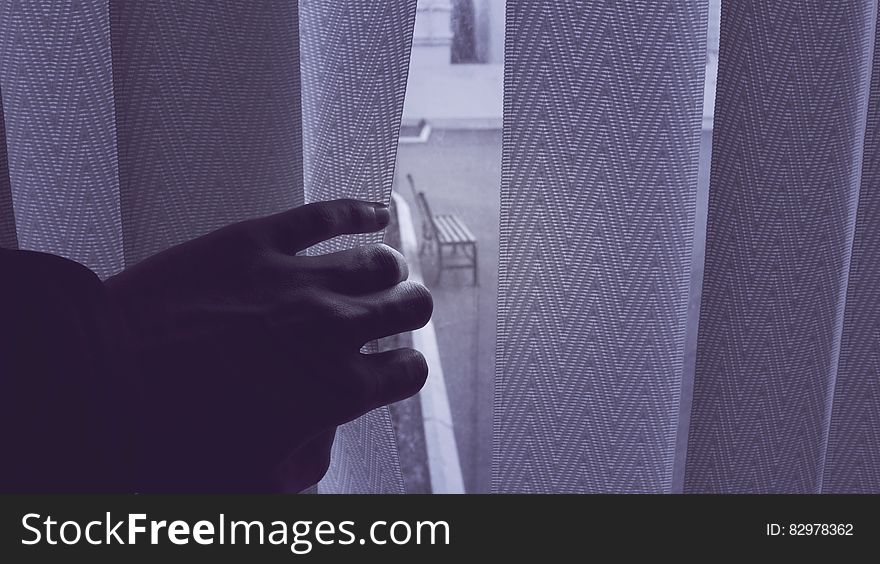A view of an empty wooden bench through vertical blinds on a window. A view of an empty wooden bench through vertical blinds on a window.