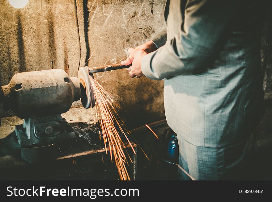 Close up of man in business suit working metal grinder inside factory. Close up of man in business suit working metal grinder inside factory.