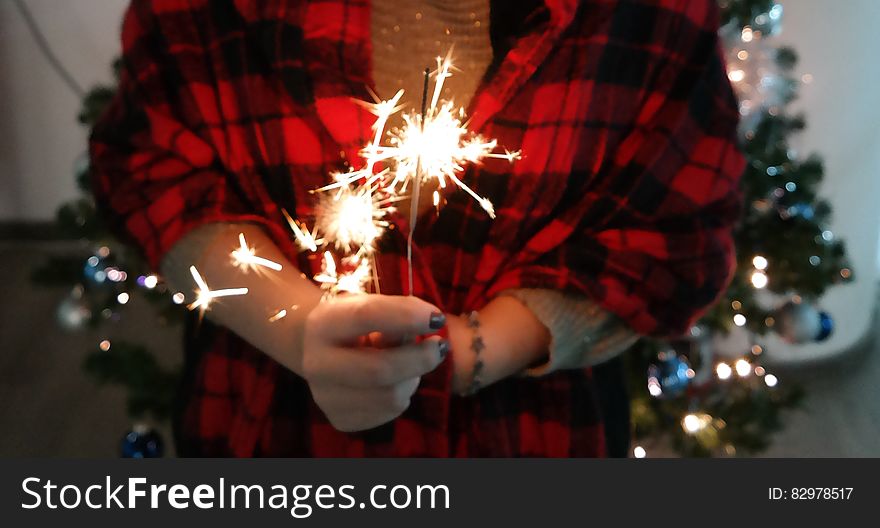 Hand holding sparkler indoors with Christmas tree in background.