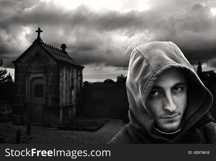 Man in hoodie jacket standing next to vault in cemetery in black and white. Man in hoodie jacket standing next to vault in cemetery in black and white.