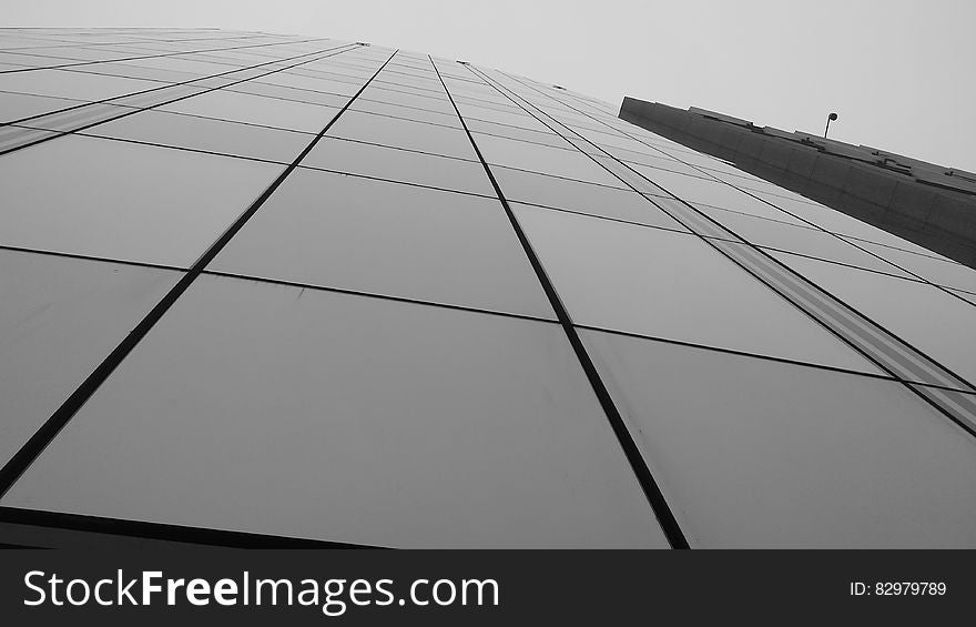 Glass panel front of modern skyscraper against overcast skies in black and white. Glass panel front of modern skyscraper against overcast skies in black and white.