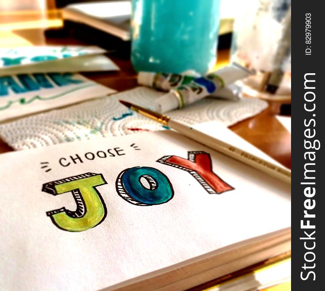 Choose joy illustrated on white paper with paintbrush and paints on tabletop.