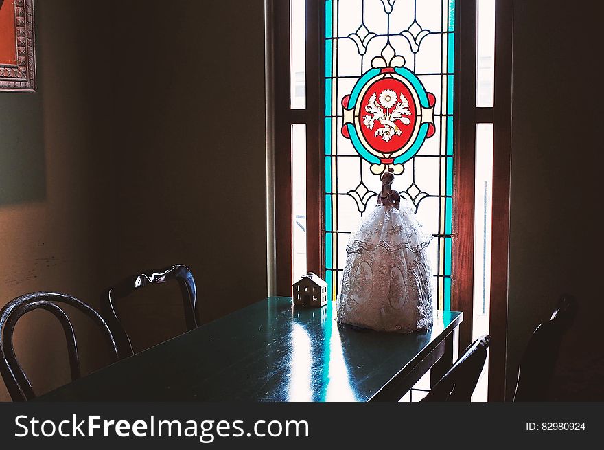 Dolls on wooden table inside room with stained glass panel in window. Dolls on wooden table inside room with stained glass panel in window.