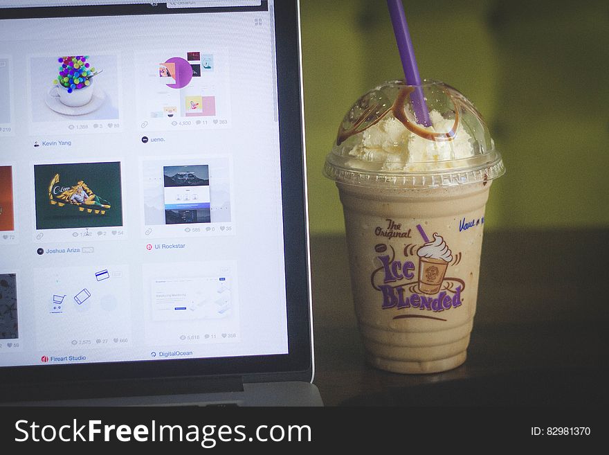 Iced coffee drink in plastic cup next to laptop computer screen. Iced coffee drink in plastic cup next to laptop computer screen.