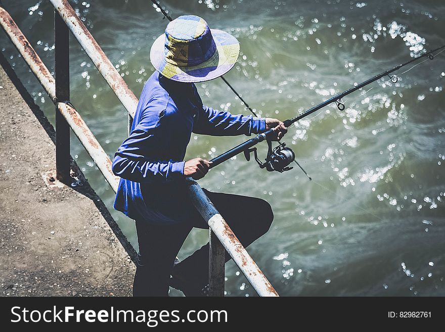 Person in Blue Long Sleeve Shirt and Black Pants Using Fishing Rod