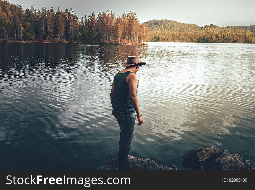 Man standing on banks of tree lines lake on sunny day. Man standing on banks of tree lines lake on sunny day.