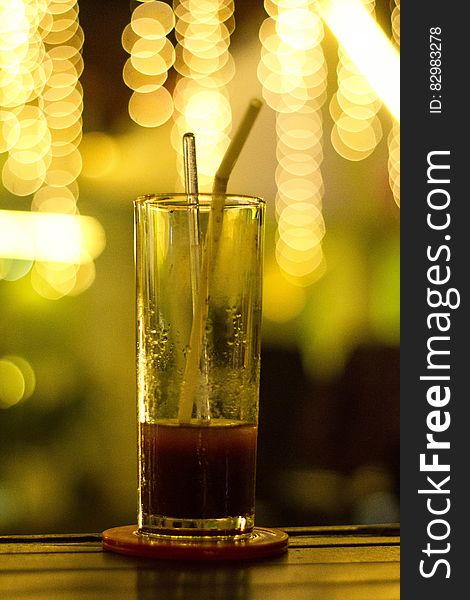 Glass with red beverage and straw on coaster on bar with bokeh lights. Glass with red beverage and straw on coaster on bar with bokeh lights.