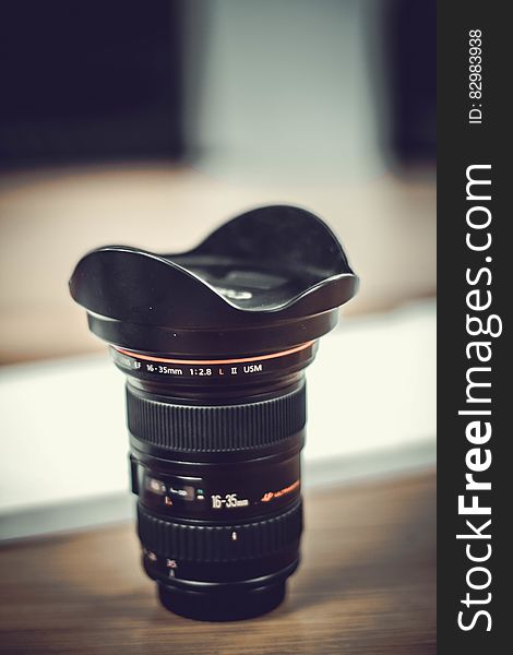 Close up of Canon lens with hood on wooden table. Close up of Canon lens with hood on wooden table.