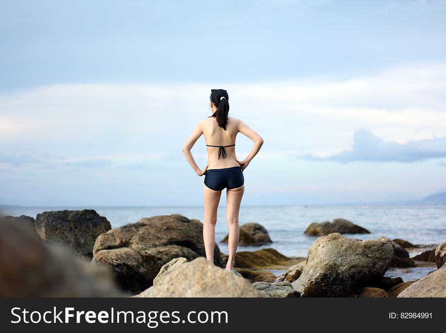 A young woman in bikini standing on a sea rock. A young woman in bikini standing on a sea rock.