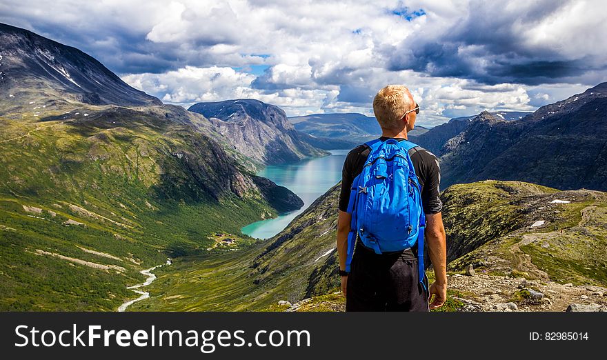 A hiker with a backpack on a mountain peak in Norway and a view of the slopes and a lake in the distance. A hiker with a backpack on a mountain peak in Norway and a view of the slopes and a lake in the distance.