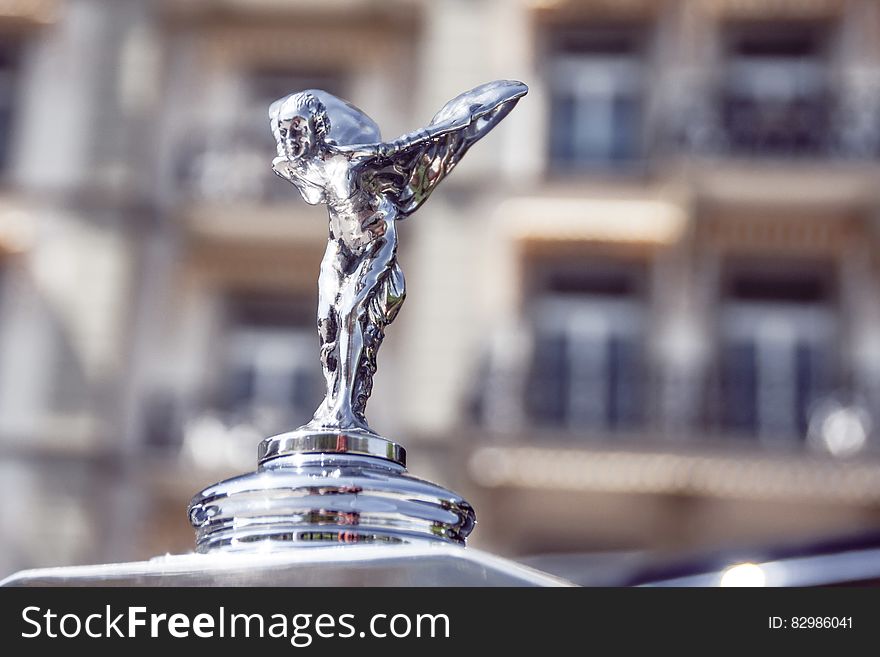 Close up of silver hood ornament on limousine outdoors on sunny day.