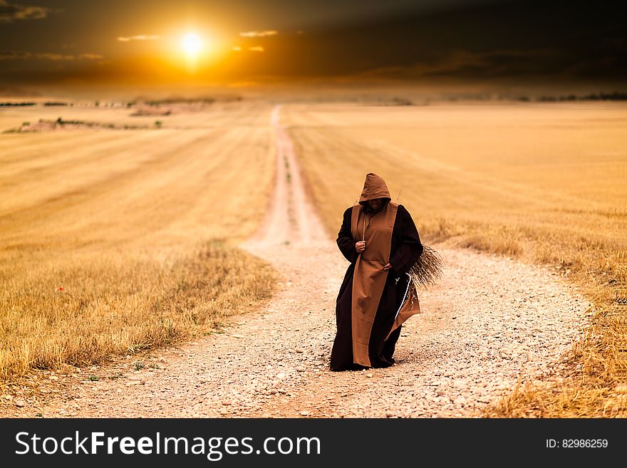 Person in Brown and Black Robe in the Middle of the Road