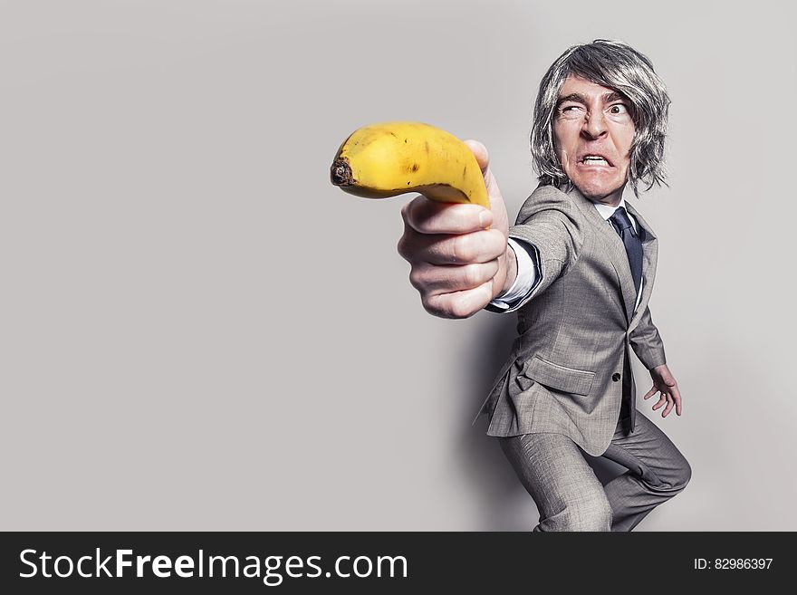 Man in Gray Suit Jacket Holding Yellow Banana Fruit While Making Face