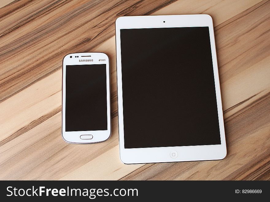 Blank touchscreen on Samsung smartphone and tablet on wooden desk. Blank touchscreen on Samsung smartphone and tablet on wooden desk.