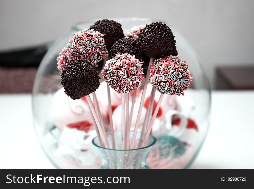 Close up of cake pops on sticks covered in sprinkles in glass vase. Close up of cake pops on sticks covered in sprinkles in glass vase.