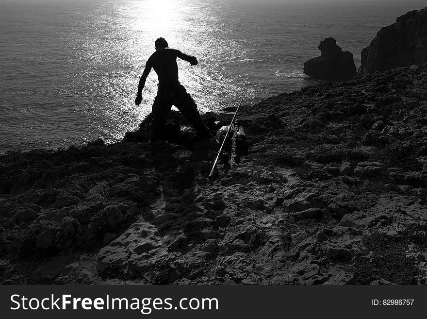 Silhouette of fisherman on rocky shores at sunrise in black and white. Silhouette of fisherman on rocky shores at sunrise in black and white.