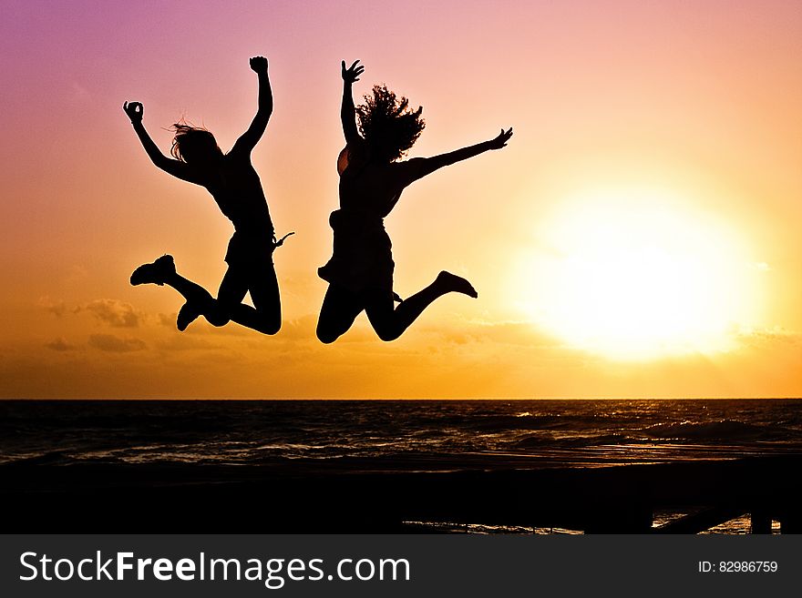 Silhouette of people jumping on beach at sunset