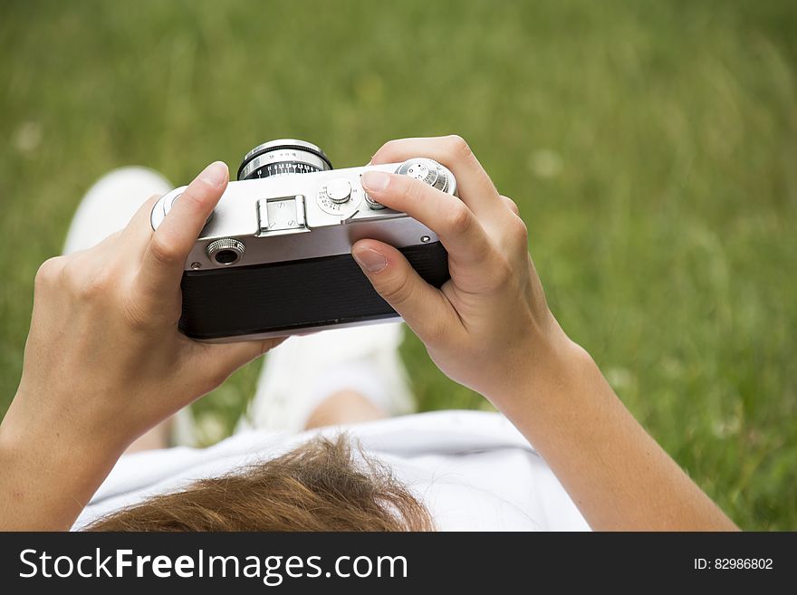 Person in White Dress Holding Grey and Black Camera on Grassland