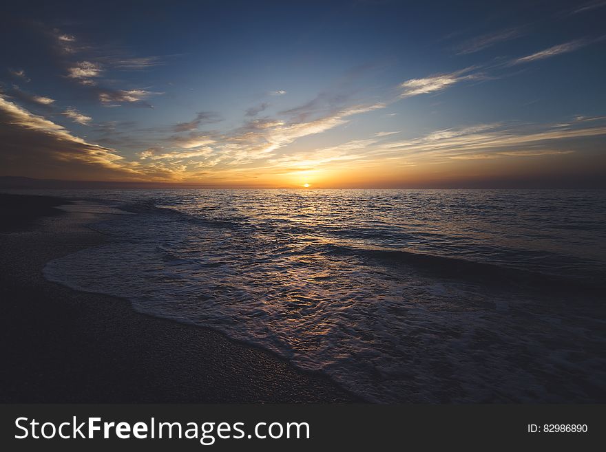Panoramic view of waves breaking on beach at sunset.