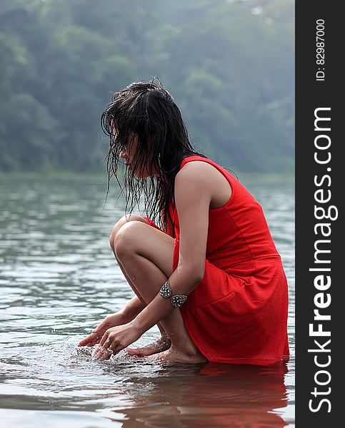 Woman In Red Dress Crouching In Lake