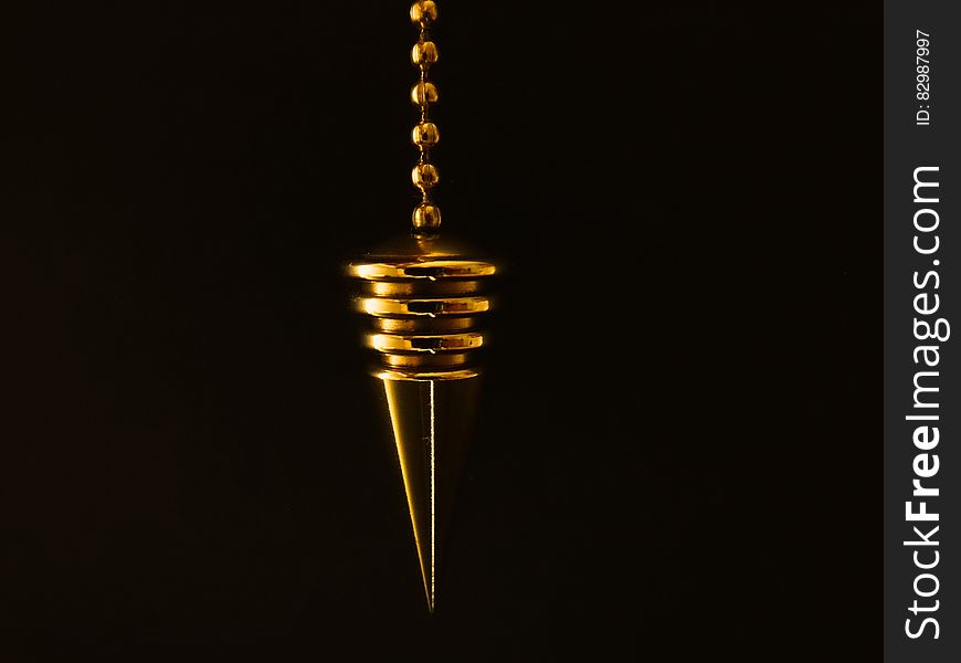 A close up of a gold pendulum on a black background.