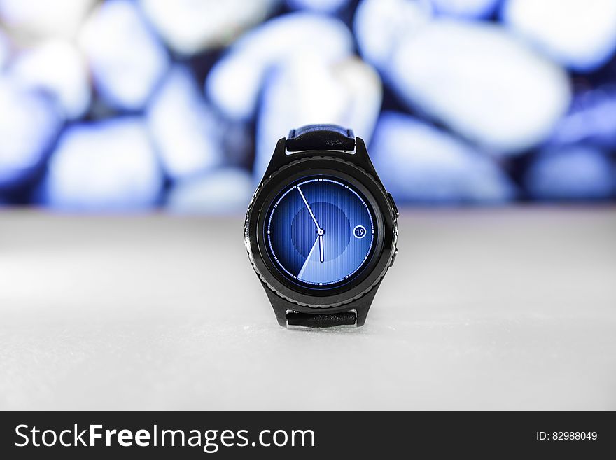 Well designed digital watch with hands pointing to five minutes to 6 o'clock with selective focus, matching blue and white background.