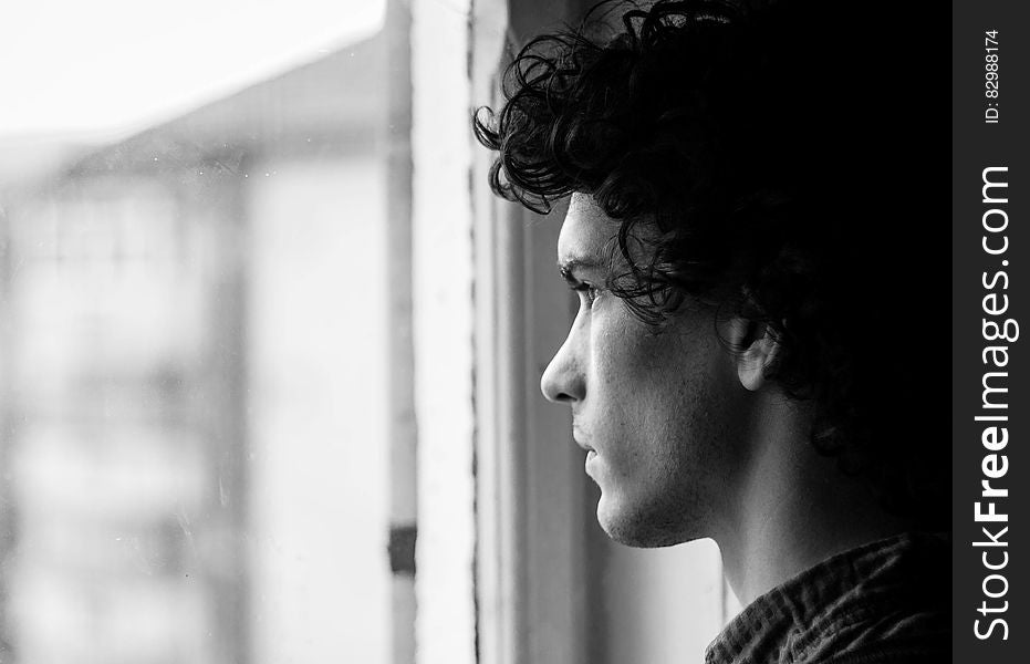 A young man looking pensively through a window. A young man looking pensively through a window.