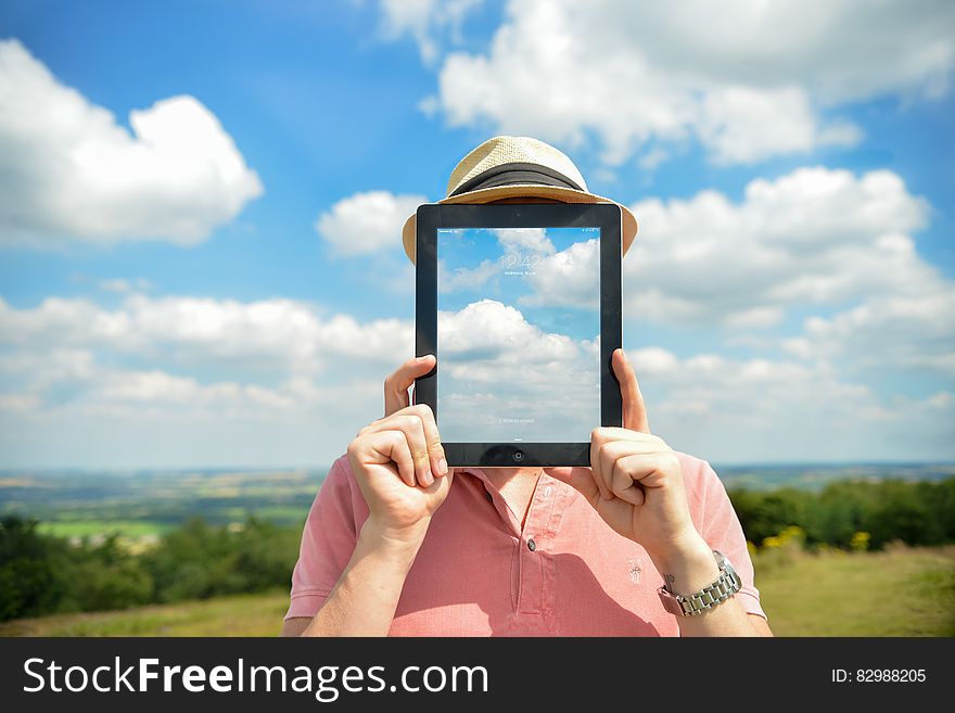 A portrait of a man outdoor holding an iPad in front of his face, with a sky wallpaper over his face. A portrait of a man outdoor holding an iPad in front of his face, with a sky wallpaper over his face.