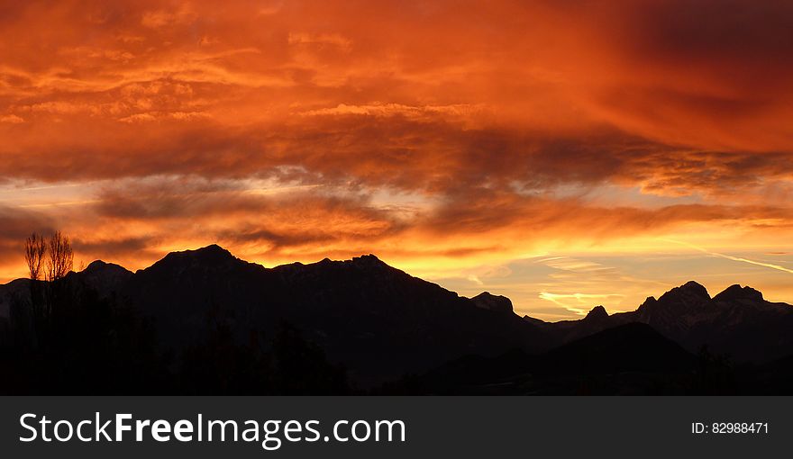 Mountain range in silhouette with dramatic orange and yellow sky at sunrise. Mountain range in silhouette with dramatic orange and yellow sky at sunrise.