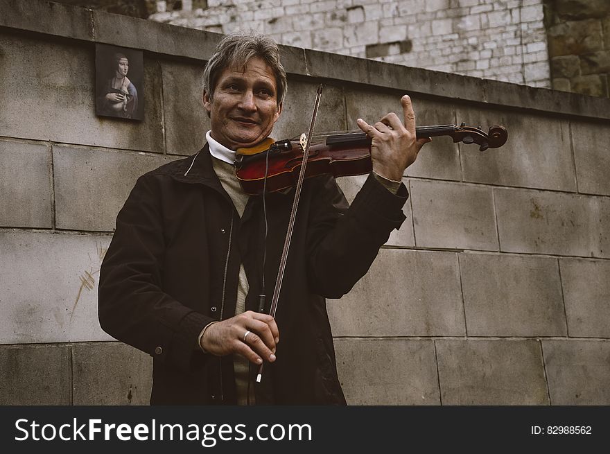 Smiling Standing Man Playing Violin by Gray Stone Wall