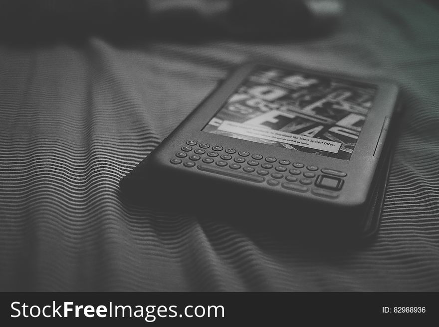 Close up of Kindle e-reader on bed in black and white. Close up of Kindle e-reader on bed in black and white.