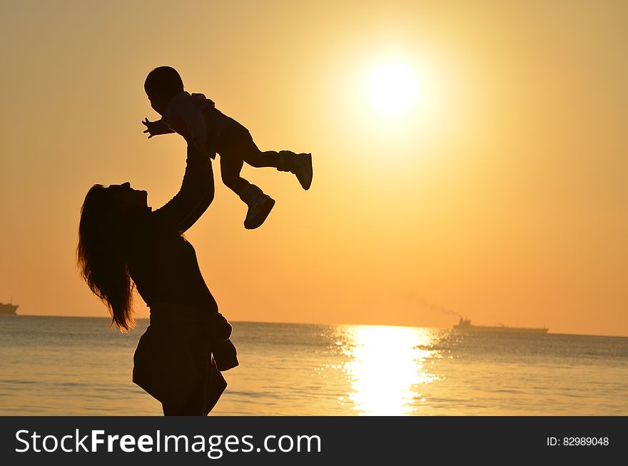 Woman Carrying Baby at Beach during Sunset