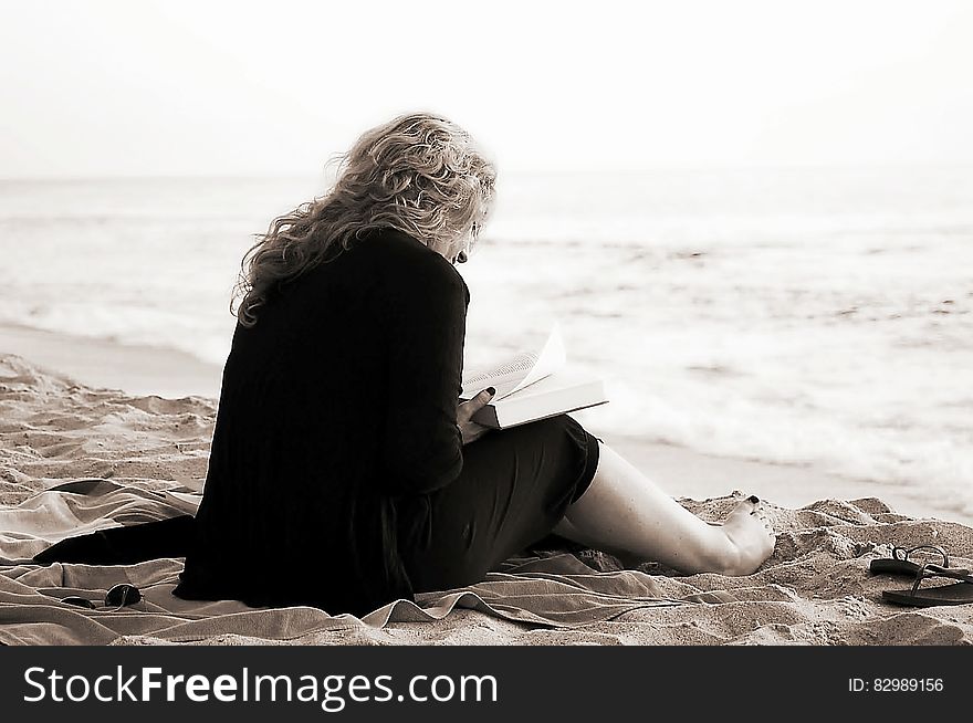 Person Sitting on the Seashore While Reading a Book