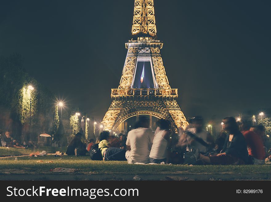People gathered sitting on the grass by the illuminated Eiffel tower at night. People gathered sitting on the grass by the illuminated Eiffel tower at night.