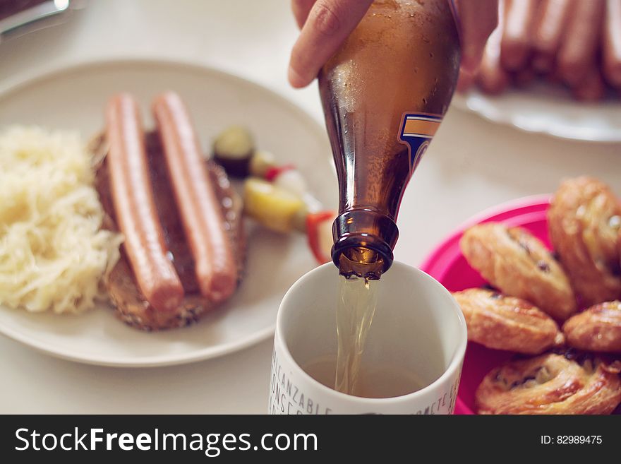 Close up of beer pouring from bottle to glass on table with German sausages and sauerkraut. Close up of beer pouring from bottle to glass on table with German sausages and sauerkraut.