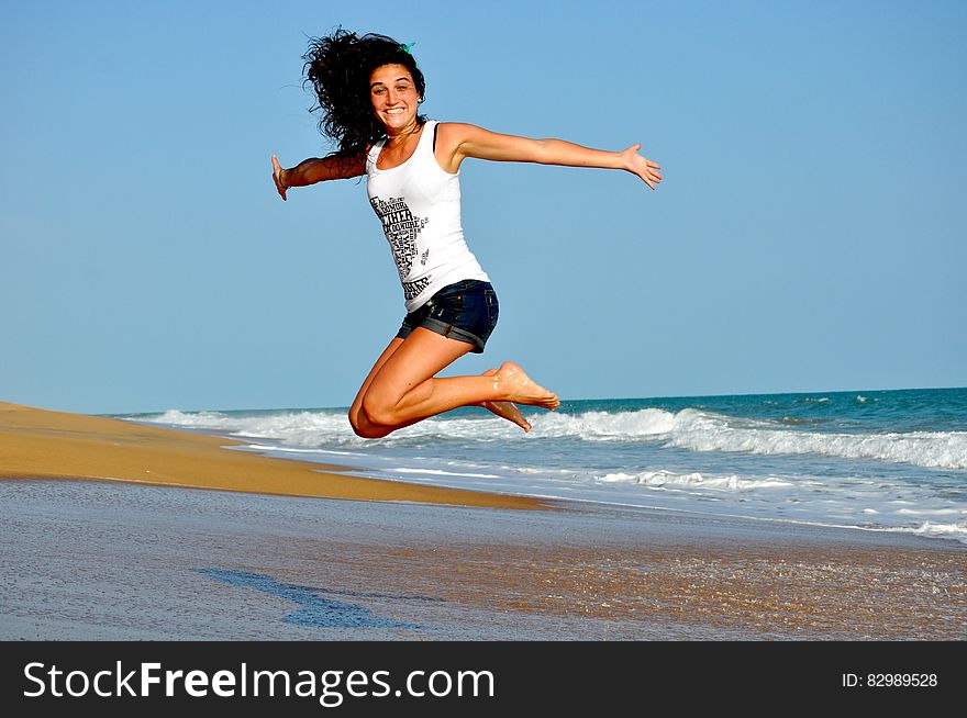 Woman in White Tanktop Jump over Beach Sand