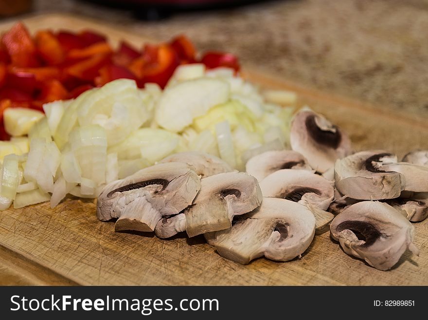 Close up of sliced mushrooms, onions and red peppers on wooden cutting board. Close up of sliced mushrooms, onions and red peppers on wooden cutting board.