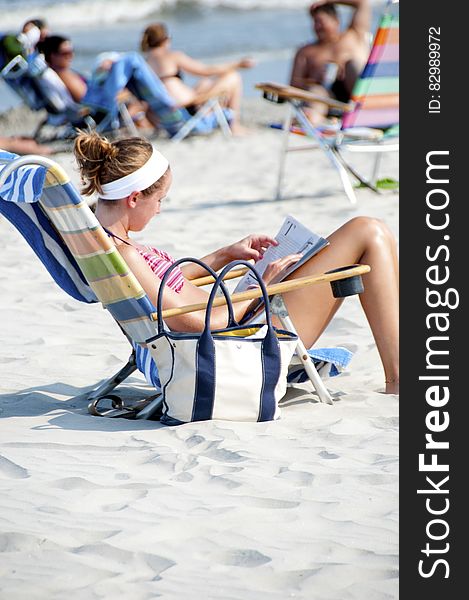 Woman Sitting On The Lounge Chair Reading Magazine On The Beach During Nighttime