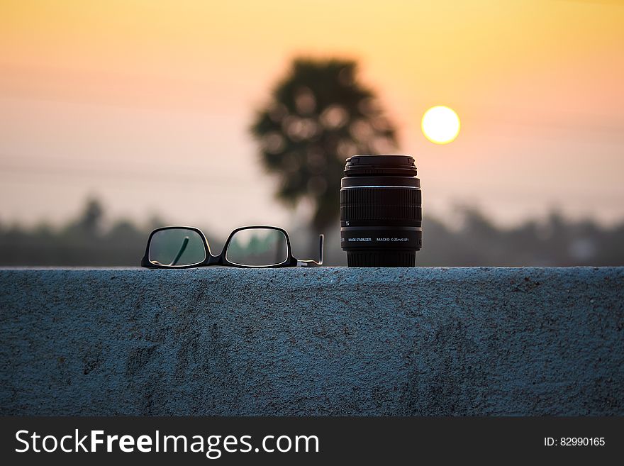Camera lens and eyeglasses on stone wall at sunset. Camera lens and eyeglasses on stone wall at sunset.