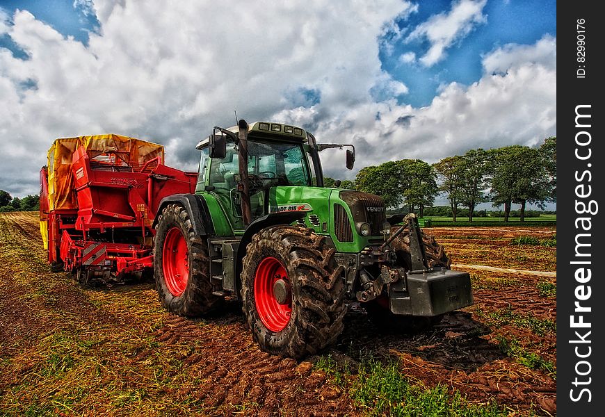 Green Tractor Pulling Red Bin On Field At Daytime