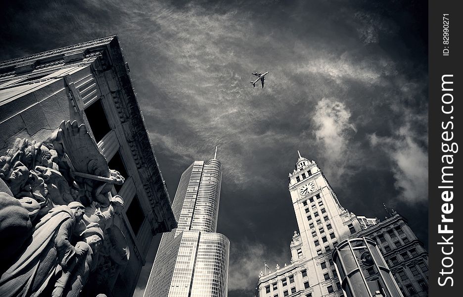 Air Plane Flying over Concrete Buildings and Statues in Grayscale Photography