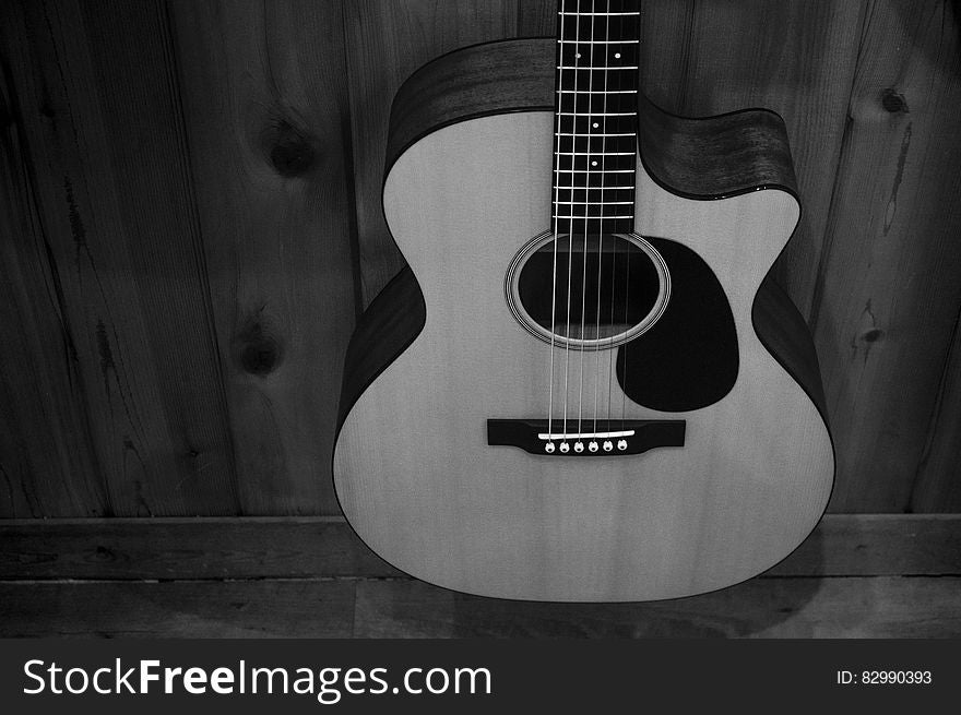 Greyscale Photo of Acoustic Guitar on Wooden Fence