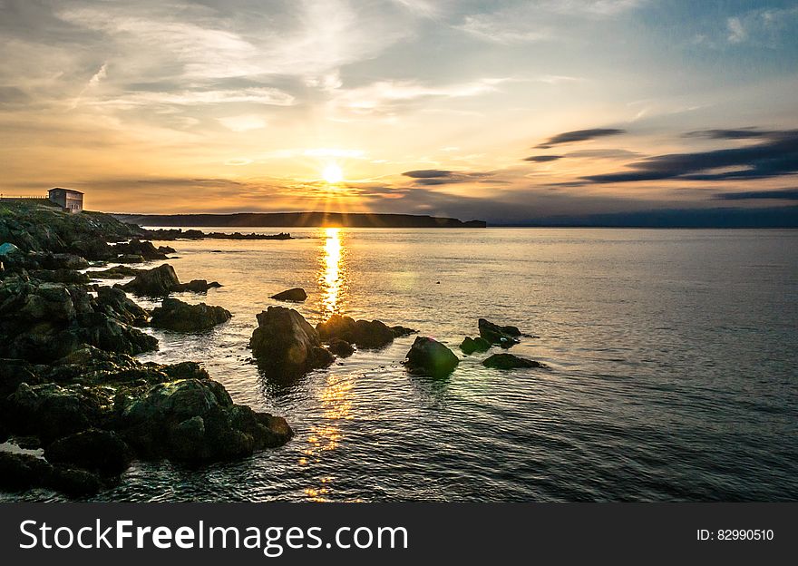 Scenic view of sunset over rocky ocean coastline with cloudscape background.