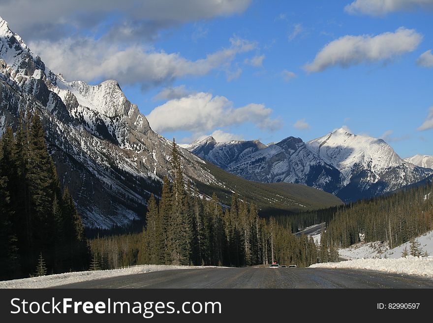 Empty alpine road through mountain peaks against blue skies on sunny day. Empty alpine road through mountain peaks against blue skies on sunny day.