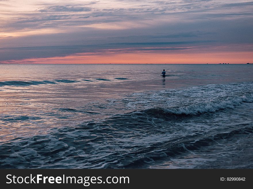 Person Standing in the Sea during Sunset