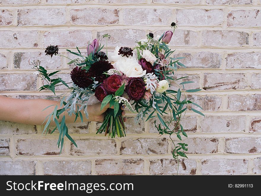 Hand holding bouquet of flowers outdoors against brick wall on sunny day. Hand holding bouquet of flowers outdoors against brick wall on sunny day.